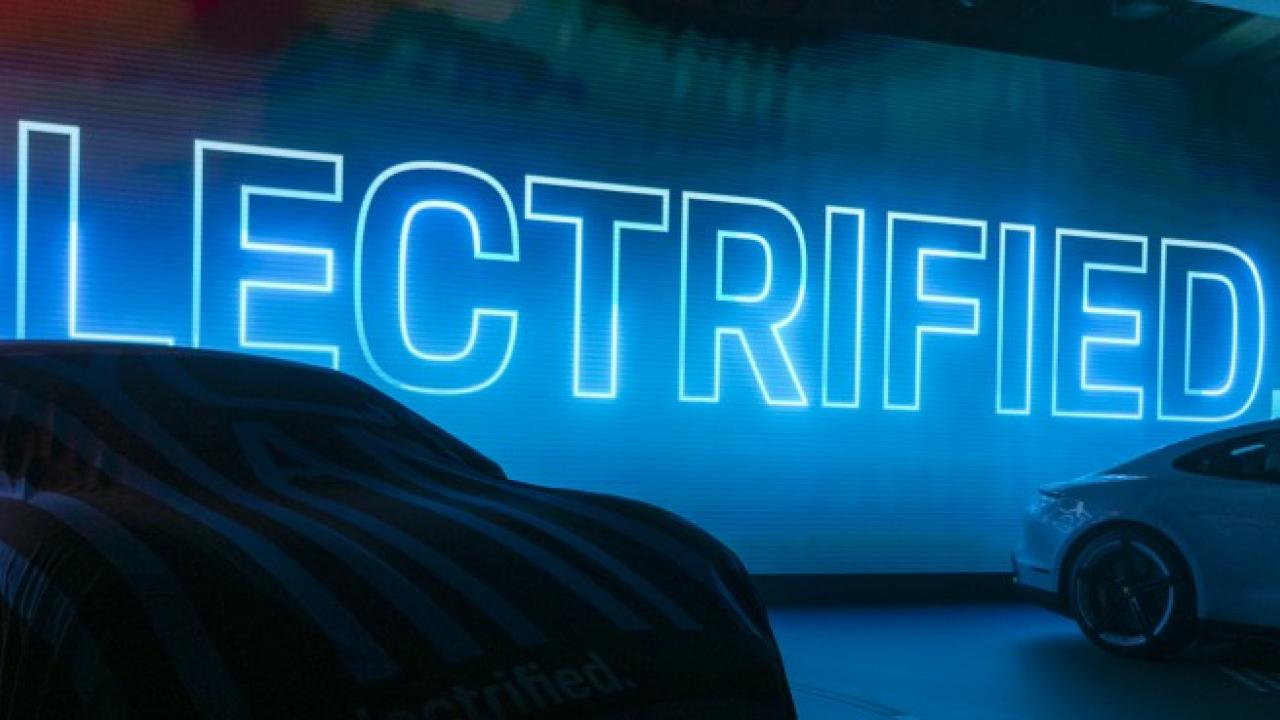 Neon blue sign of the word "ELECTRIFIED" behind the silhouette of two display vehicles